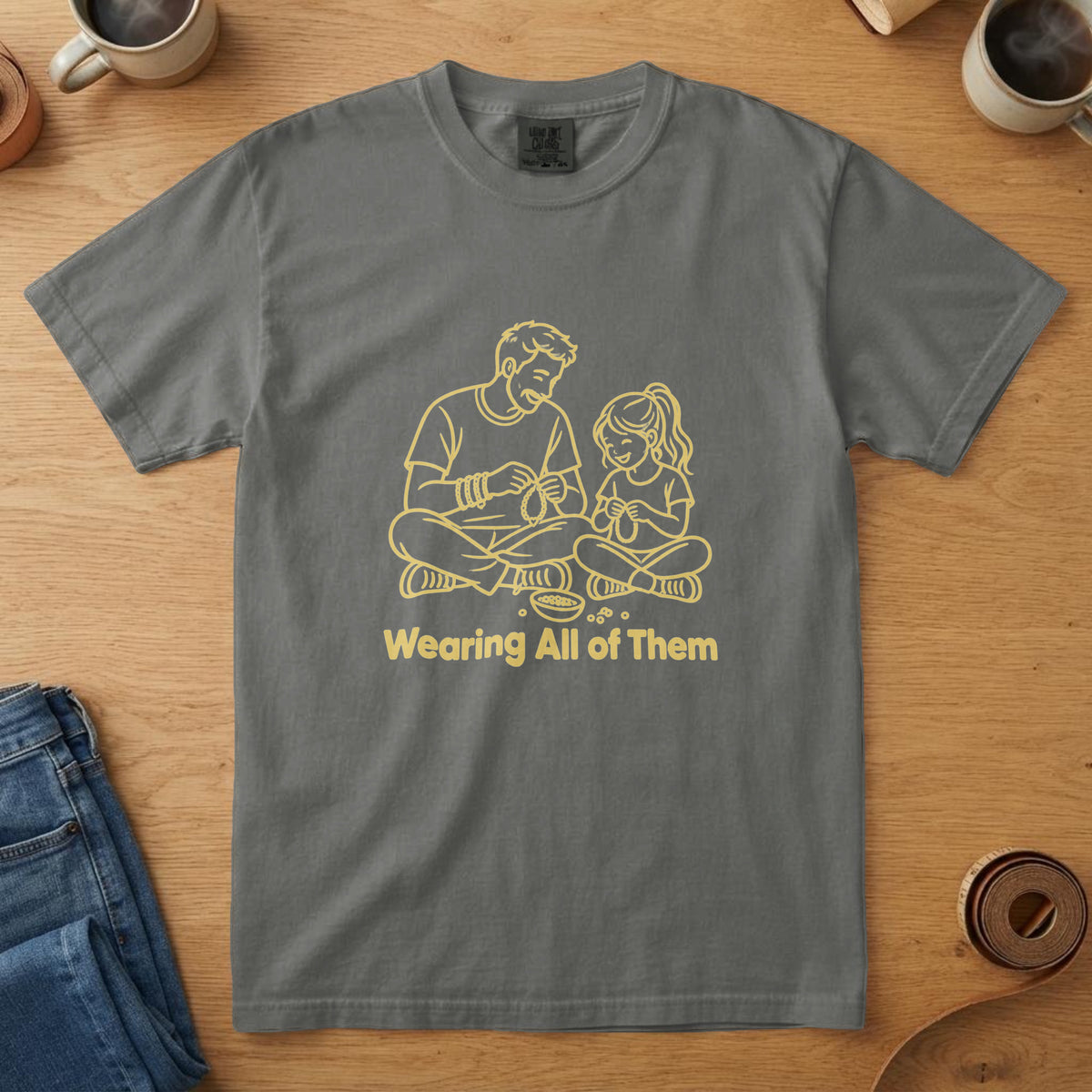 Pepper t-shirt with a yellow line drawing of a dad and daughter making bracelets and the words "Wearing All of Them"