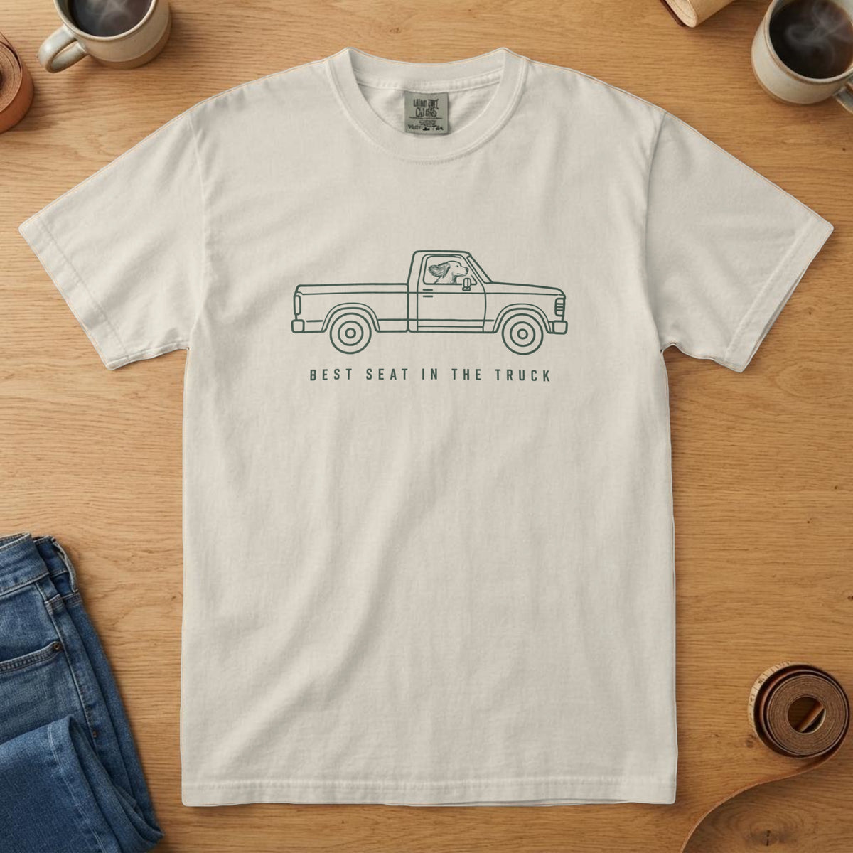 Ivory t-shirt with a forest line drawing of a pickup truck with a dog out the window and "Best Seat in the Truck"
