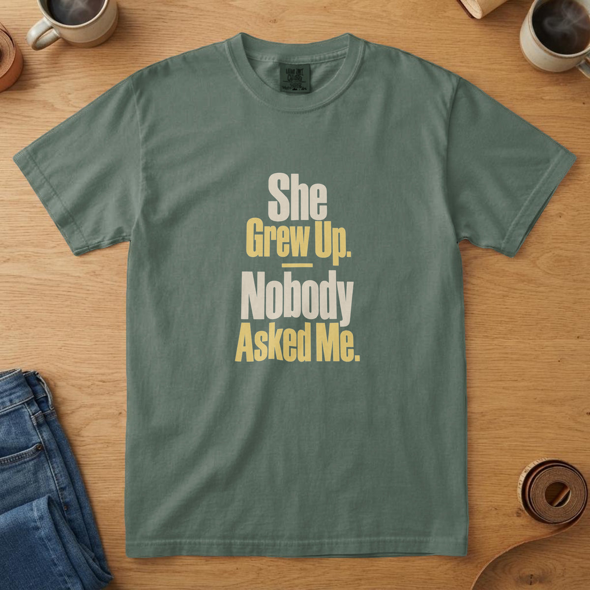 Blue Spruce t-shirt with tall bone and yellow type and the words "She Grew Up. Nobody Asked Me."