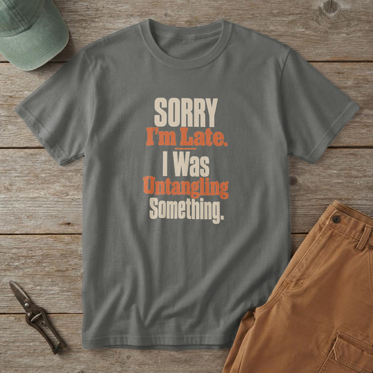 Pepper t-shirt with bold cream and orange type reading "Sorry I'm Late. I Was Untangling Something.", on a picnic table