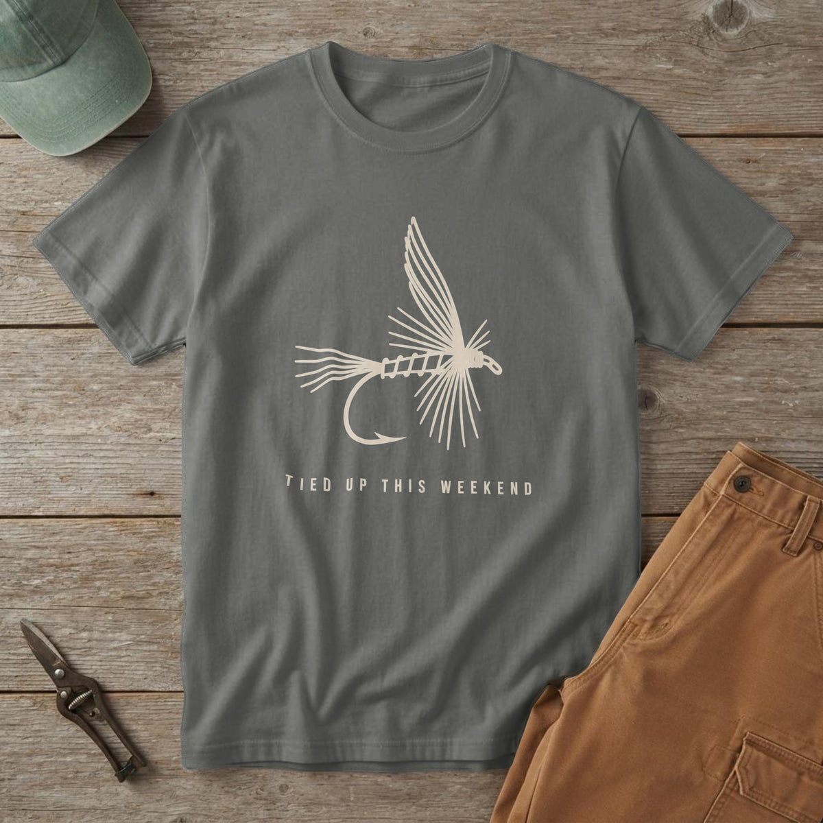 Pepper t-shirt with a cream dry-fly line drawing and the words "Tied Up This Weekend", on a cedar picnic table