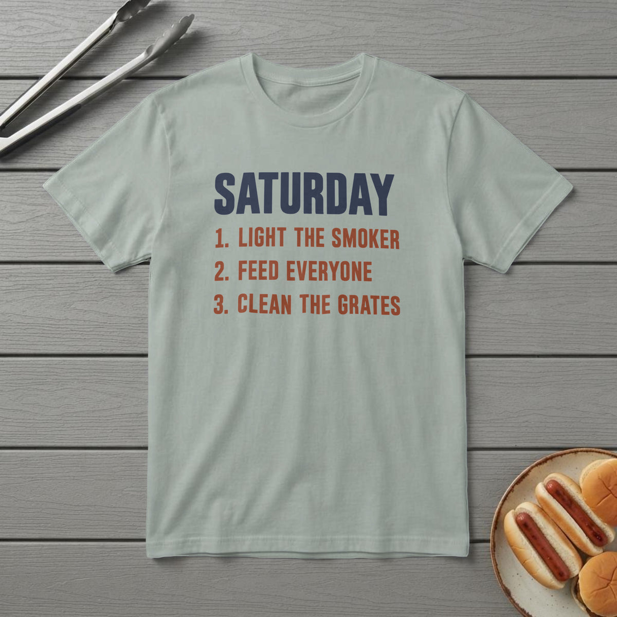 Bay t-shirt with a navy and rust list reading "Saturday: 1. Light the smoker 2. Feed everyone 3. Clean the grates"