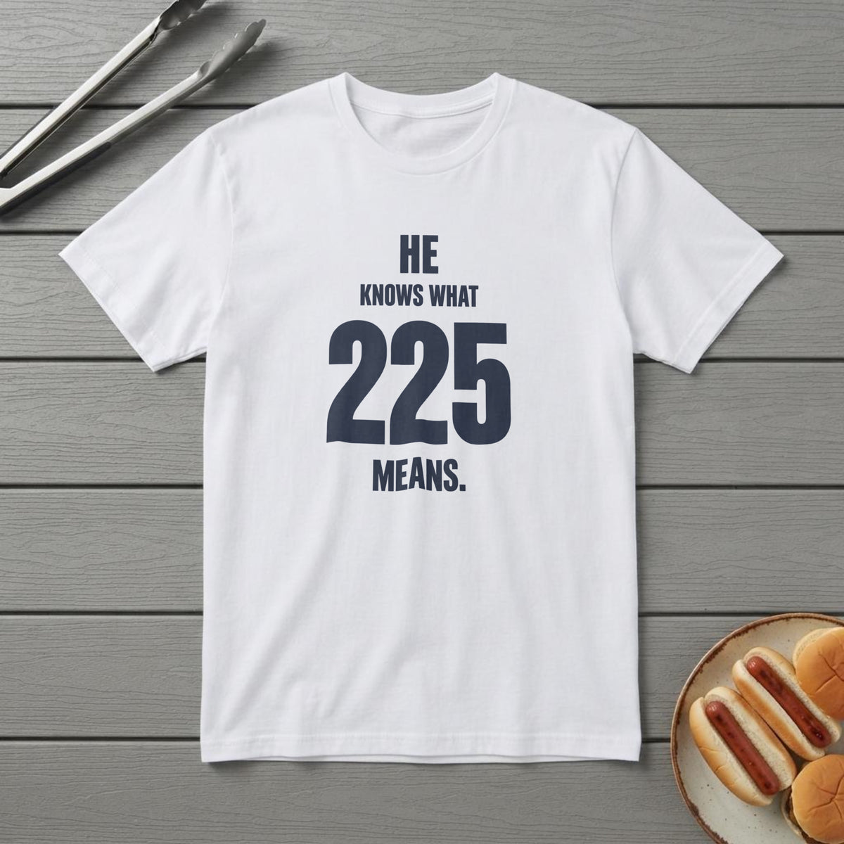 White t-shirt with navy type reading "He Knows What 225 Means." with a large 225, on a grey deck