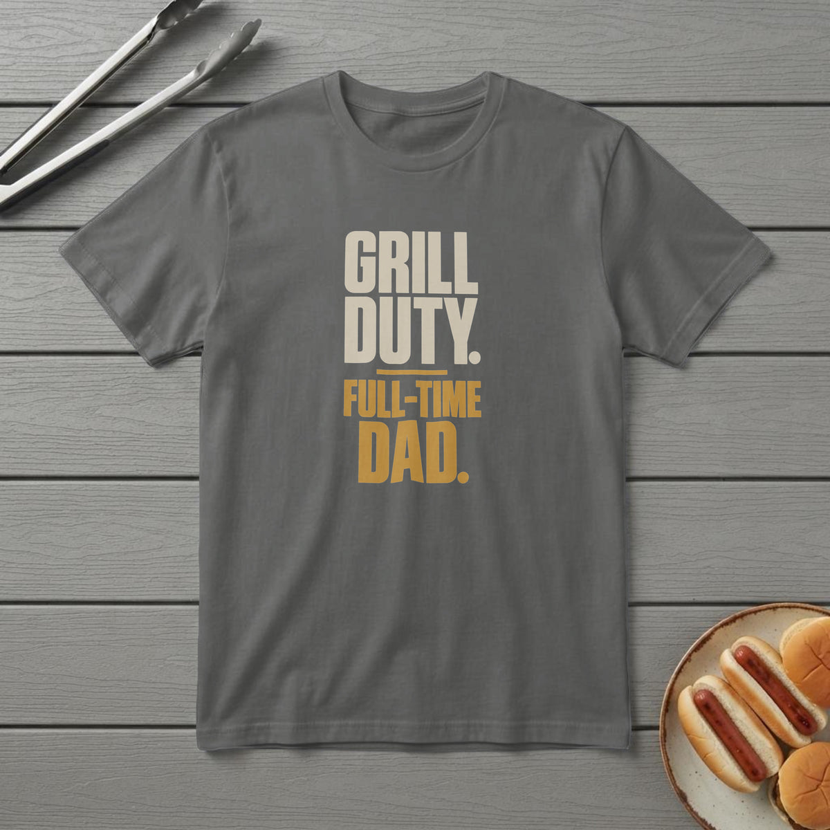 Pepper t-shirt with bold cream and mustard type reading "Grill Duty. Full-Time Dad.", on a grey deck