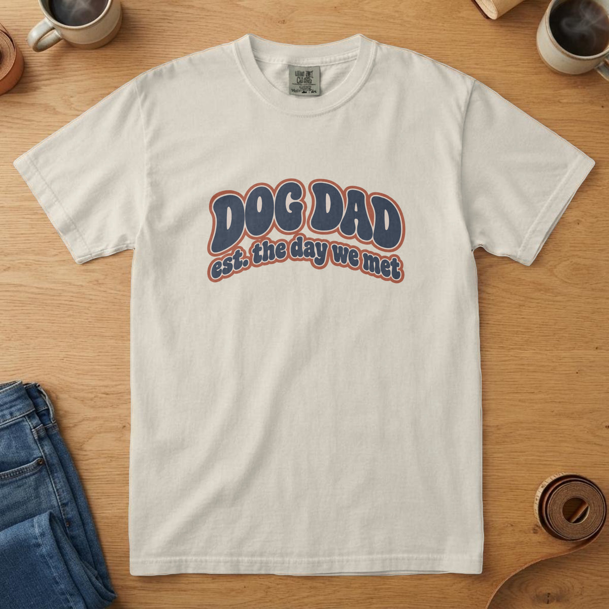 Ivory t-shirt with navy and rust 70s-style puff lettering reading "DOG DAD est. the day we met"