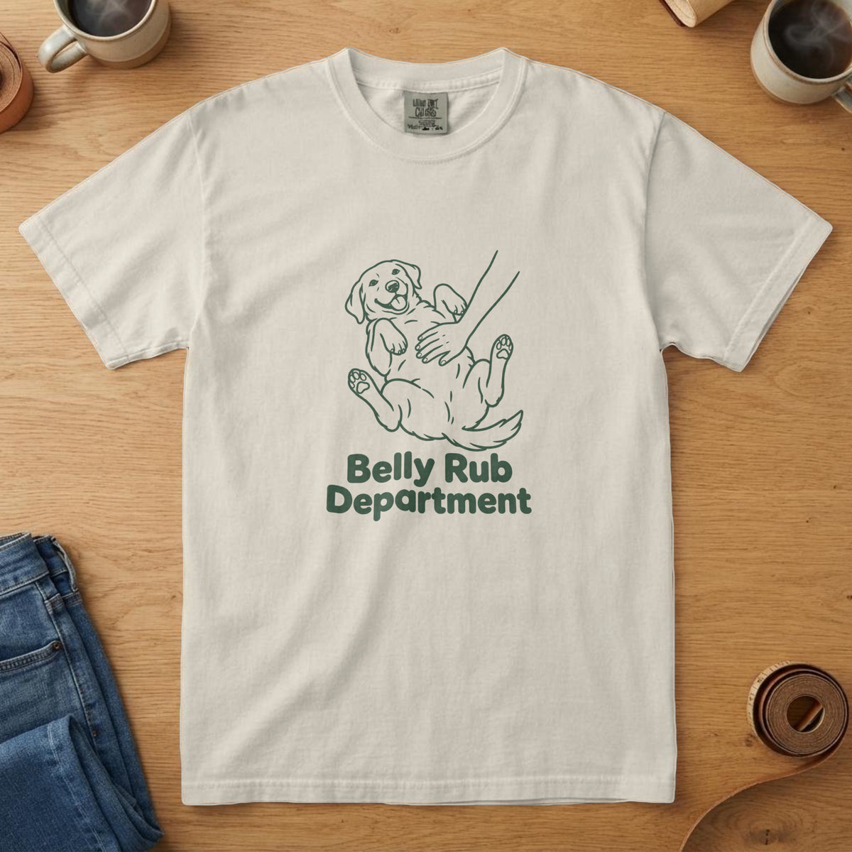 Ivory t-shirt with a forest line drawing of a dog on its back getting a belly rub and the words "Belly Rub Department"