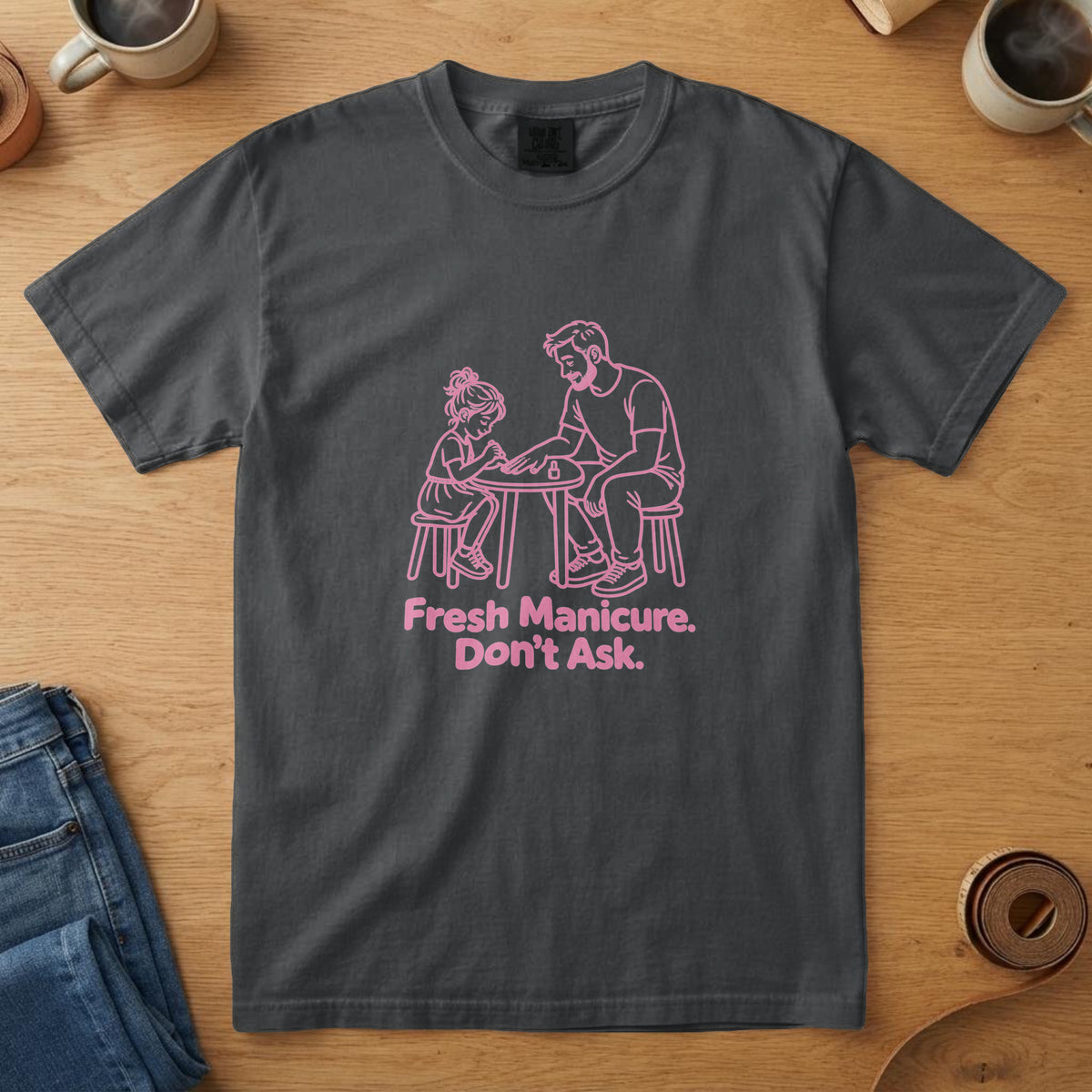 Black t-shirt with a pink line drawing of a girl painting her dad's nails and the words "Fresh Manicure. Don't Ask."