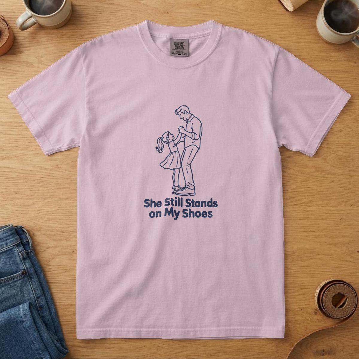 Blossom t-shirt with a navy line drawing of a girl dancing on her dad's shoes and the words "She Still Stands on My Shoes"